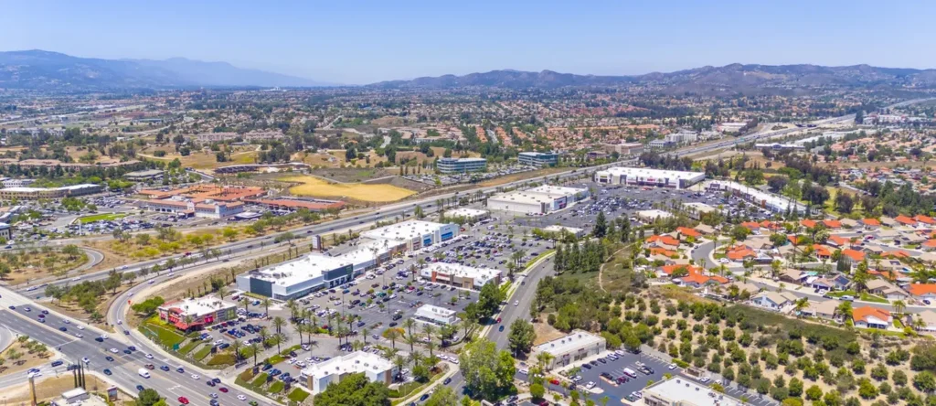 Aerial view of a suburban commercial district with parking lots, roads, and surrounding residential areas.