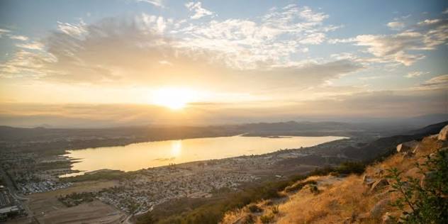 Sunset over a lake with a town below and rolling hills in the foreground, warm golden light filling the sky.
