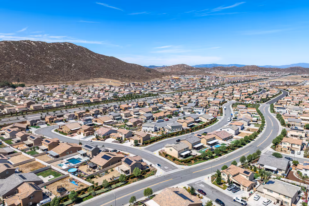 A suburban neighborhood with winding streets, single-family homes, and desert hills under a bright blue sky.